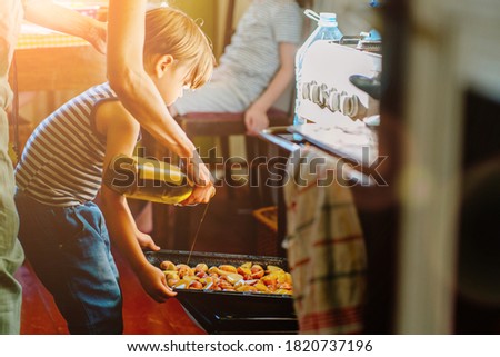 Cute little preschooler boy in striped t-shirt help his mother at kitchen. Cook at home. Young woman pouring oil at a baking tray before oven. Her son helping hold. Family cooking dinner together
