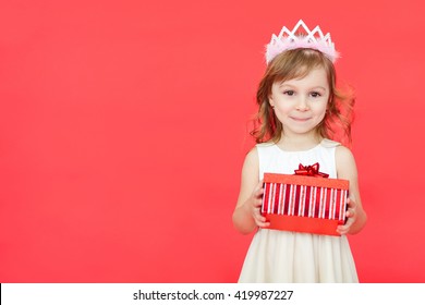 Cute little preschooler girl christmas portrait, isolated on red. Child girl wearing crown and white dress holding a red gift box  isolated over red background - Powered by Shutterstock