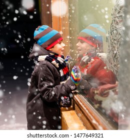 Cute Little School Kid Boy On Christmas Market. Funny Happy Child In Fashion Winter Clothes Making Window Shopping Decorated With Gifts, Xmas Tree. Holidays, Christmas, Childhood And People Concept