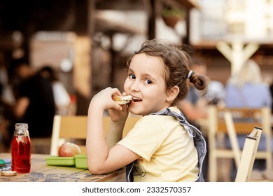 Cute little schoolgirl eating from lunch box outdoor sitting on a school cafeteria. Food for kids - Powered by Shutterstock