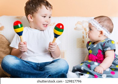 Cute little sister and her brother sitting with maracas on sofa