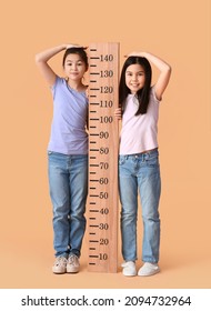 Cute little sisters measuring height on color background