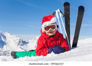 Cute Little Skier In Santa's Hat Laying On Snow