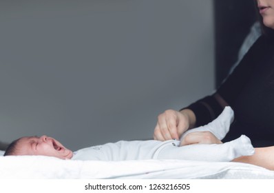 Cute Little Sleepy Newborn Baby Crying While Mom Is Dressing Her Up In Onesie On Table