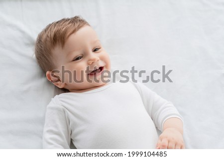 Cute little small child caucasian infant toddler newborn smiling with baby milk teeth lying on the comfortable bed. Teething concept, childcare and parenthood. Copy space