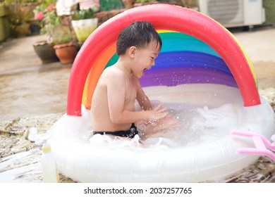 Cute Little Smiling Asian 5 Years Old Toddler Boy Child Having Fun Splashing In Inflatable Swimming Pool, Playing Alone In Backyard In Sunny Morning, Hot Summer Day, Fun Things To Do At Home Concept