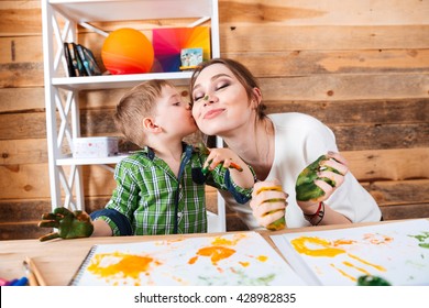 Cute little son kissing his mother and having fun using paints 库存照片