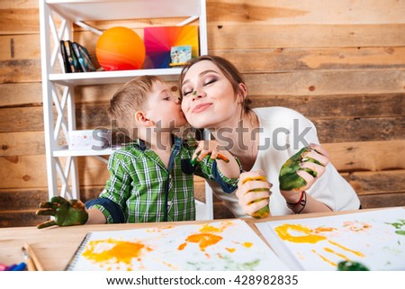 Cute little son kissing his mother and having fun using paints
