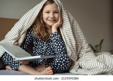Cute little teen child girl sitting and reading book on bed under the blanket 