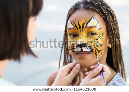 Cute little tiger. African-american girl getting face painting outdoors, having fun, copy space