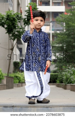 Cute little toddler in Blue Bandhani kurta and white dhoti. Holding Dandiya in hand for playing garba in navratri festival. Indian boy in traditional outfit for festive season. 