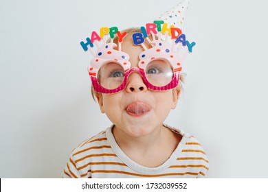 Cute little toddler boy in happy birthday glasses and party hat sticking his tongue out over white. - Powered by Shutterstock