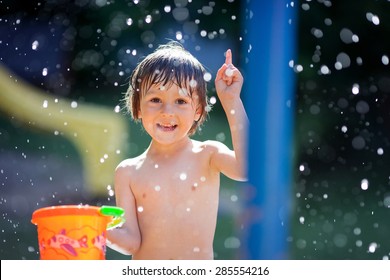 Cute little toddler boy, having fun with splashed water shot during summer time, holding bucket, outdoors