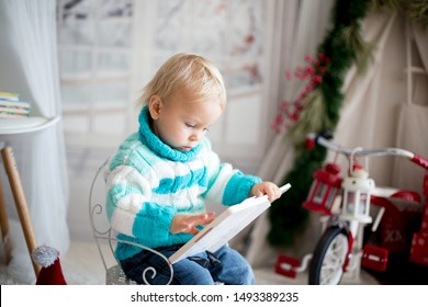 Cute Little Toddler Child With Colorful Book At Home On A Snowy Winter Day, Christmas Decoration