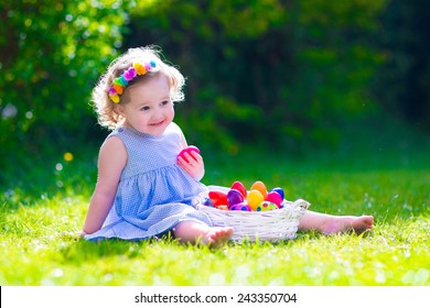 Cute little toddler girl with curly hair wearing a blue summer dress having fun during Easter egg hunt relaxing in the garden on a sunny spring day - Powered by Shutterstock