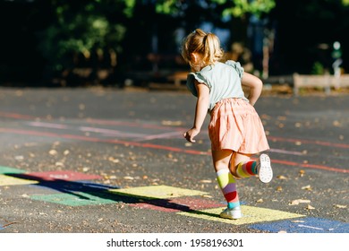 Cute little toddler girl playing hopscotch game drawn with colorful chalks on asphalt. Little active child jumping on playground outdoors on a sunny day. Summer activities for children. - Shutterstock ID 1958196301