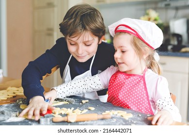 Cute Little Toddler Girl And Preteen Kid Boy Baking Easter Cookies At Home Indoors. Children, Siblings With Apron And Chef Hat Cut Out Bunny Cookie In Domestic Kitchen. Brother And Sister In Love