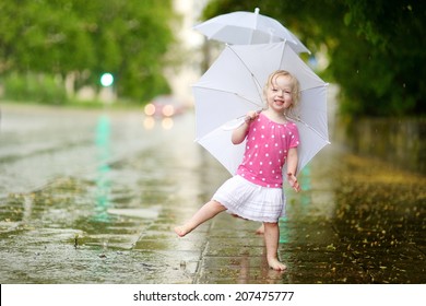 Cute little toddler girl standing in a puddle holding umbrella on a rainy summer day