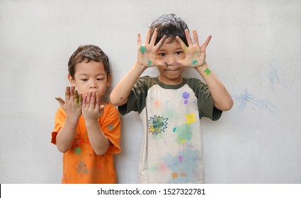 Cute Little Two Asian Boys Brotherhood Play Fun Colors In Activity Creativity Time, Showing Stain Hands And Clothes. Kids Have Eye Color And Dark Brown Hair.