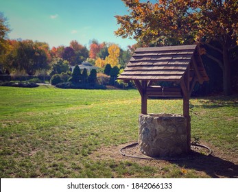 Cute Little Water Well Wishing Well Made Of Stone With A Wooden Top In A Field In Autumn In New England Massachusetts With Colorful Foliage And Trees Of Color And Sun Light. 