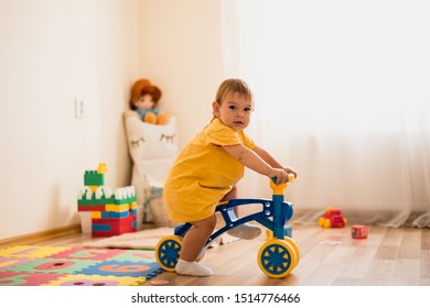 Cute Lovely Small Baby Girl Learning To Balance On Her First Bike At Home. Toddler Activity At Daycare