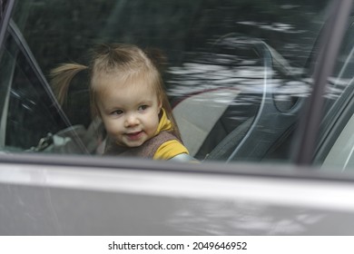 Cute and lovely toddler girl, sitting on a backseat, looking through a car window