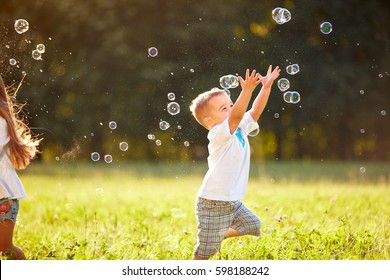 Cute male child catches soap bubbles in nature