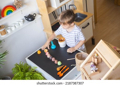 Cute Male Kid Preparing Toy Food Boiling Vegetables On Cooker At Childish Room Kitchen With Montessori Wooden Material. Confident Child Boy Chef Meal Cooking At Cuisine Playing Early Development Game