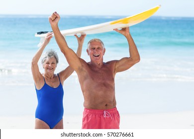 Cute mature couple holding a surfboard over their heads on the beach - Powered by Shutterstock