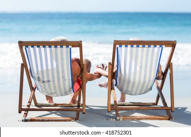 Cute mature couple lying on deckchairs on the beach