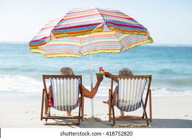 Cute mature couple lying on deckchairs on the beach