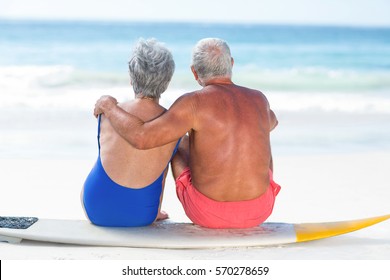 Cute Mature Couple Sitting On A Surfboard On The Beach