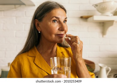 Cute mature female holding drugs and glass of water in hands. Elderly woman taking medication. Treatment course or vitamins complex idea. Healthy lifestyle and healthcare concept - Powered by Shutterstock