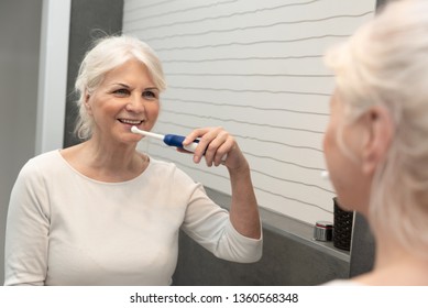 Cute Mature Woman Brushing Teeth. Electric Toothbrush Used By Senior Woman.