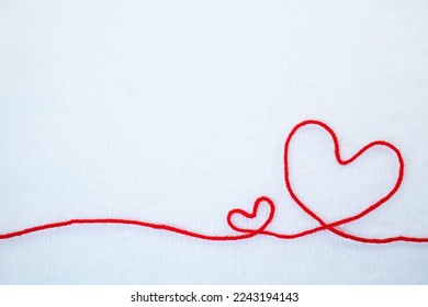 A cute message frame in the shape of a simple two large and small hearts made of a single red thread on a soft white background