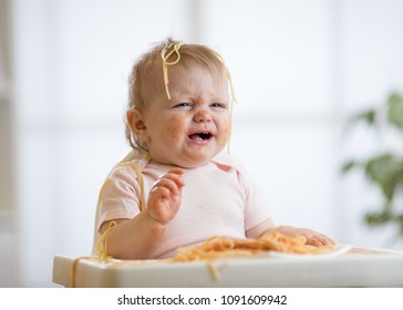 Cute messy baby girl crying while eating pasta at home
