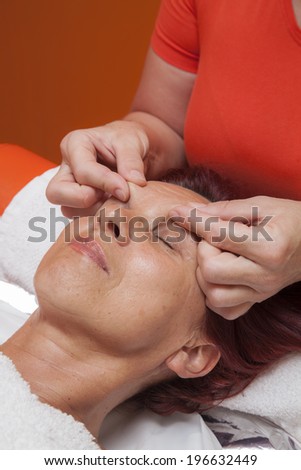 Cute mid aged woman receiving a professional therapeutic facial massage and lymphatic drainage, while lying on a towel in a award-winning health massage center, series of various techniques 