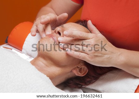 Cute mid aged woman receiving a professional therapeutic facial massage and lymphatic drainage, while lying on a towel in a award-winning health massage center, series of various techniques 