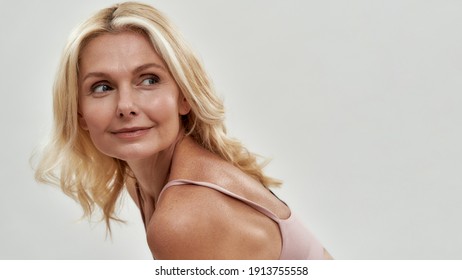 Cute middle aged caucasian woman with fair hair looking at top to side above her shoulder while posing on light background, widescreen. Authentic woman beauty concept