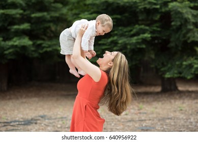 A cute millennial mother lifting her two year old toddler above her head