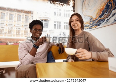 Cute mixed race couple of teenagers enjoying milkshake at cafeteria, first date