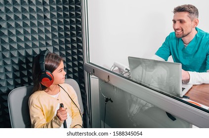 cute mixed race girl having a hearing test in a special room, she is wearing headphones, her Audiologis checking hearing