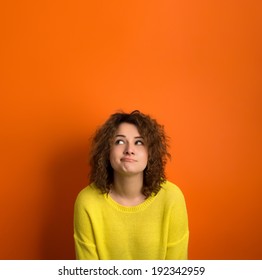 Cute Model In Yellow Sweater Among Orange Background With Funny Face. Thinking And Wondering Concepts. Lots Of Copy Space For Advertising