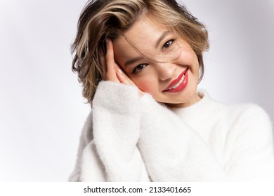 Cute modern young woman with stylish short haircut, tender makeup, ideal smooth skin, wearing white soft cozy sweater posing in studio. Skincare, make-up cosmetics advertisement.