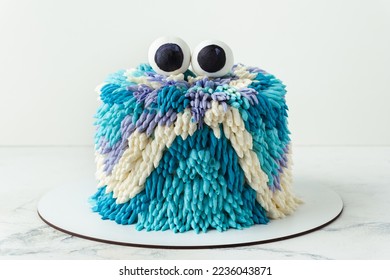 Cute monster cake on the white background. Funny birthday cake with turquoise and blue fluffy cream cheese frosting decorated with mastic edible eyes on top. Spooky kids Halloween party cake