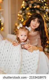 cute mother and daughter on a chair in a room with Christmas garlands. the tradition of decorating the house and dressing up for the holidays. gifts for the family. happy childhood and motherhood.