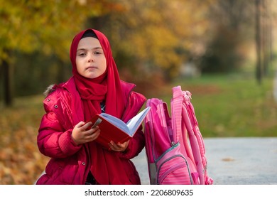 A Cute Muslim Girl Student Learning For School In The Autumn Park.