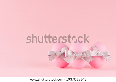 Cute and naivety easter background with pink eggs group with grey bows on pastel pink backdrop.