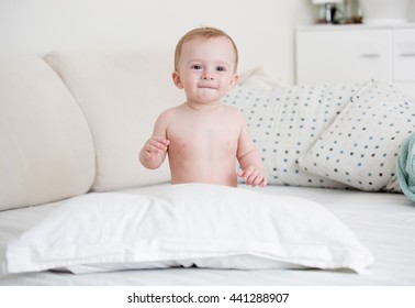 Cute Naked Baby Boy Sitting On Bed At Bedroom