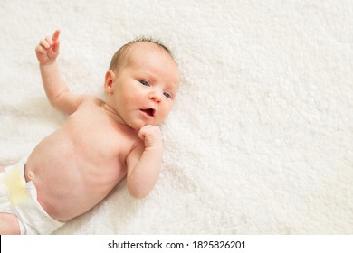 Cute Naked Newborn Baby With Open Eyes, Lying On A Bed. A Parent Holds The Legs Of A Newborn Baby.